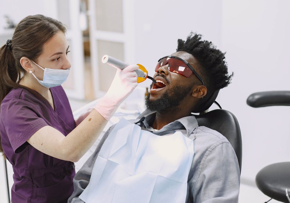 African patient in dentistry sitting in dental chair Young african-american man. Guy visiting dentist's office for prevention of the oral cavity. Man and famale doctor while checkup teeth.